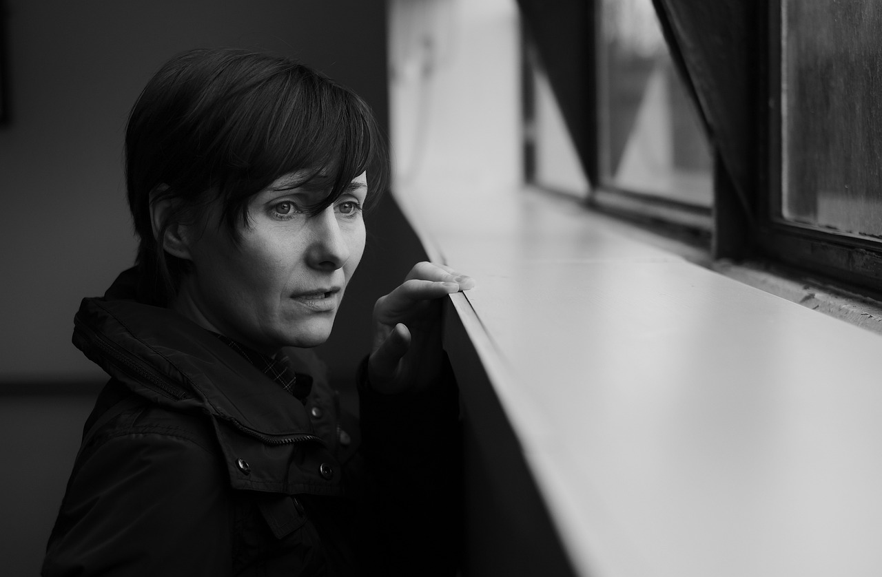 Black and white image of short haired 40ish woman gazing out window with concern